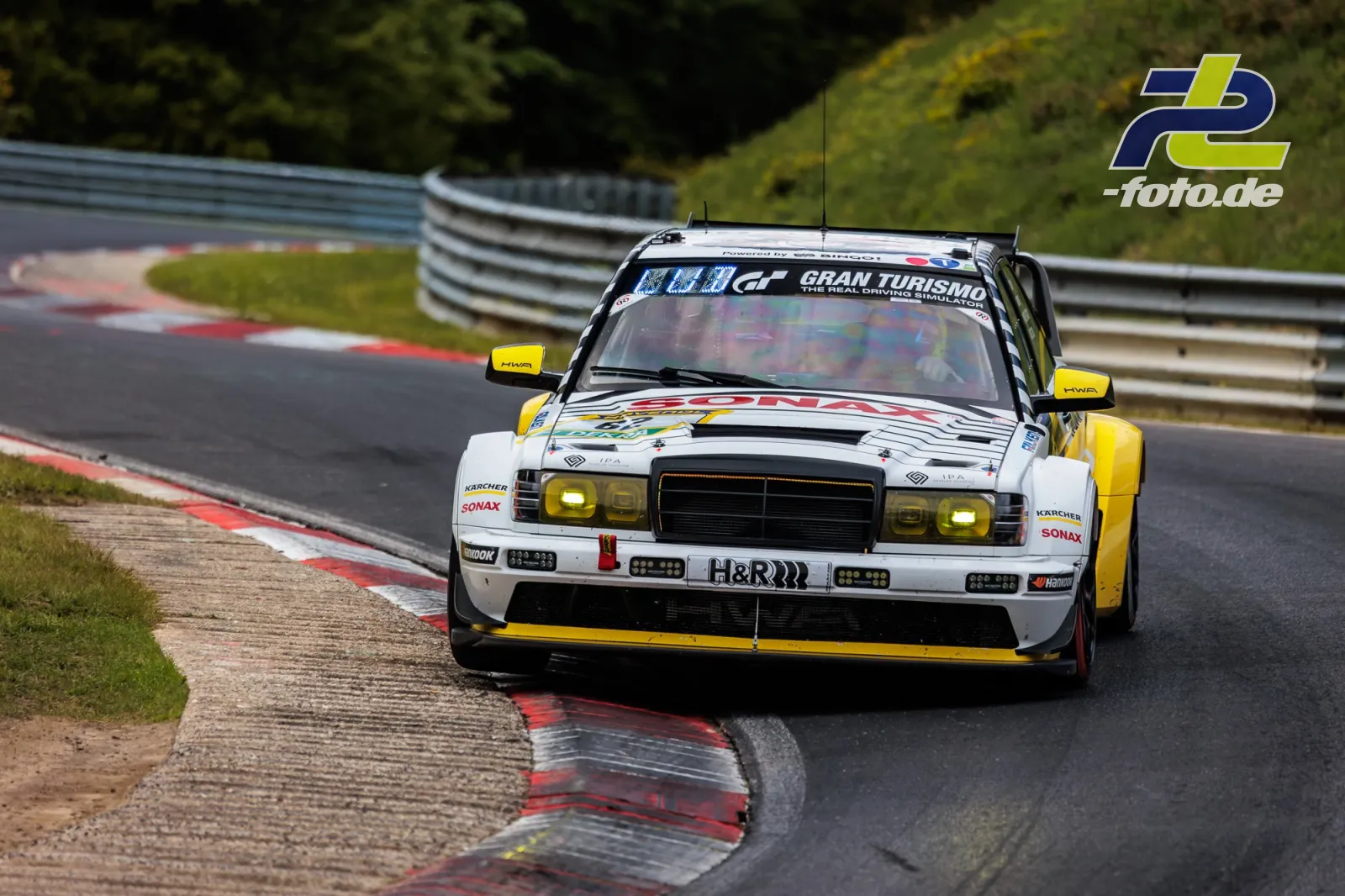 HWA EVO.R in Kurve auf dem Nürburgring während des 24h-Rennens. Weiß-gelber Rennwagen mit Sponsorenlogos auf der Nordschleife.