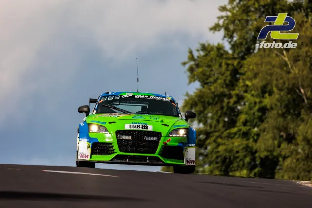 Grün-blauer Rennwagen springt über eine Kuppe auf der Nürburgring-Nordschleife während des 24h-Rennens.