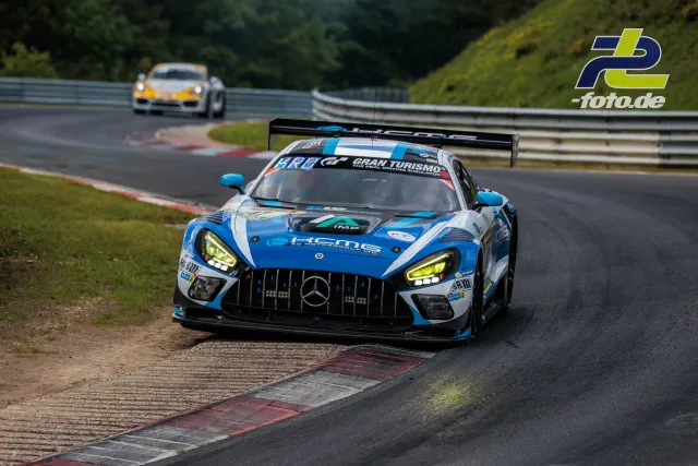 Mercedes-AMG GT3 in blau-weißer Lackierung beim 24h-Rennen auf dem Nürburgring, Kurvenausgang mit Randstein, Porsche im Hintergrund.