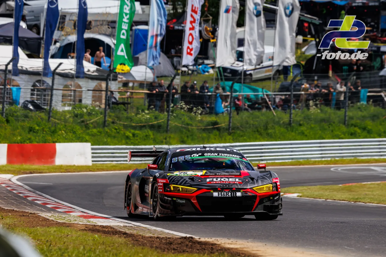 Audi R8 LMS GT3 in schwarz-roter Lackierung in einer Kurve auf der Nürburgring-Nordschleife, im Hintergrund Tribüne mit Zuschauern.