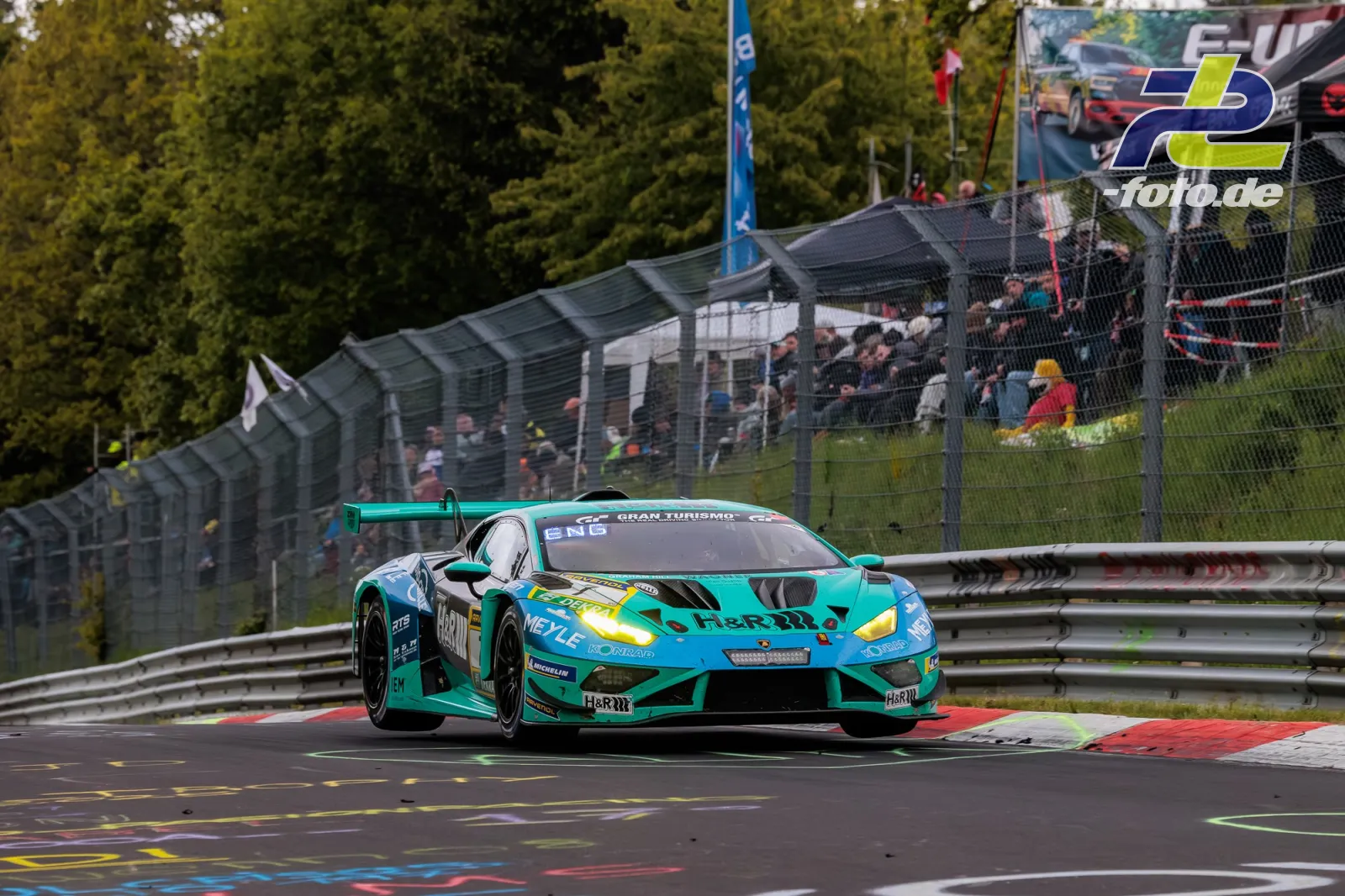 Türkis-grüner Lamborghini Huracán GT3 #7 auf der Nordschleife vor Zuschauertribüne beim 24h Rennen Nürburgring.