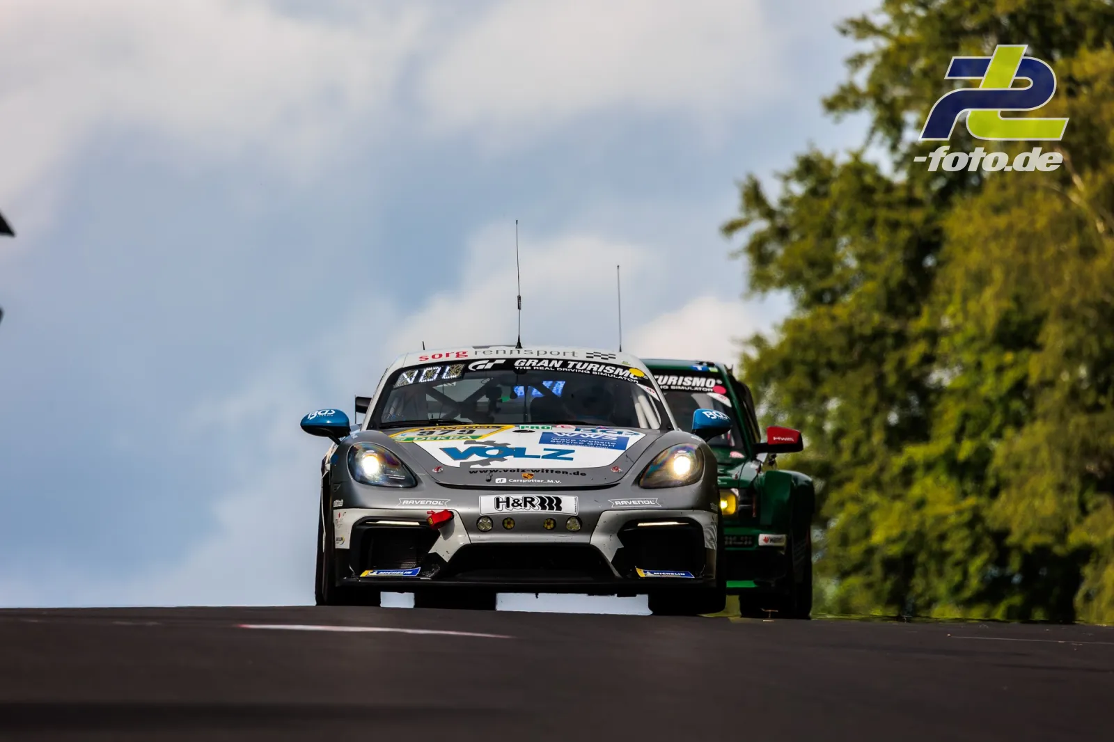 Porsche 718 Cayman GT4 Clubsport auf der Kuppe der Nordschleife beim 24h-Rennen am Nürburgring, frontale Perspektive mit eingeschalteten Scheinwerfern.