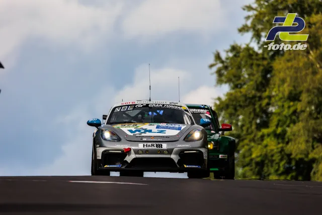 Porsche Cayman GT4 in grau-weißer Lackierung während des 24h-Rennens auf der Nordschleife, zweites Fahrzeug im Hintergrund.