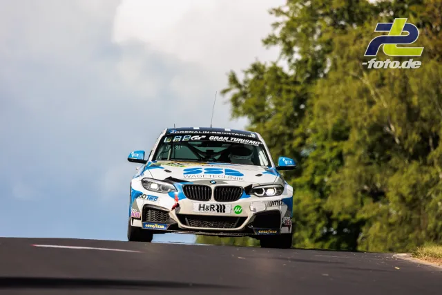 BMW M240i Racing in weißer Lackierung mit blauen Akzenten auf einer Kuppe der Nürburgring-Nordschleife beim 24h-Rennen