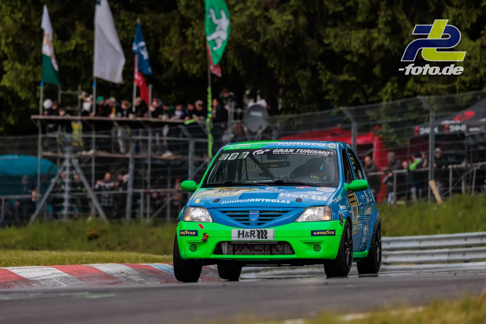Dacia Logan in Kurve beim 24h-Rennen Nürburgring, blau-grüne Lackierung, Tribüne mit Zuschauern im Hintergrund