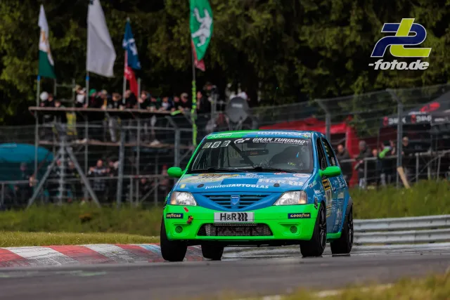 Dacia Logan in grün-blauer Lackierung auf der Nordschleife während des 24h-Rennens am Nürburgring, Tribüne im Hintergrund