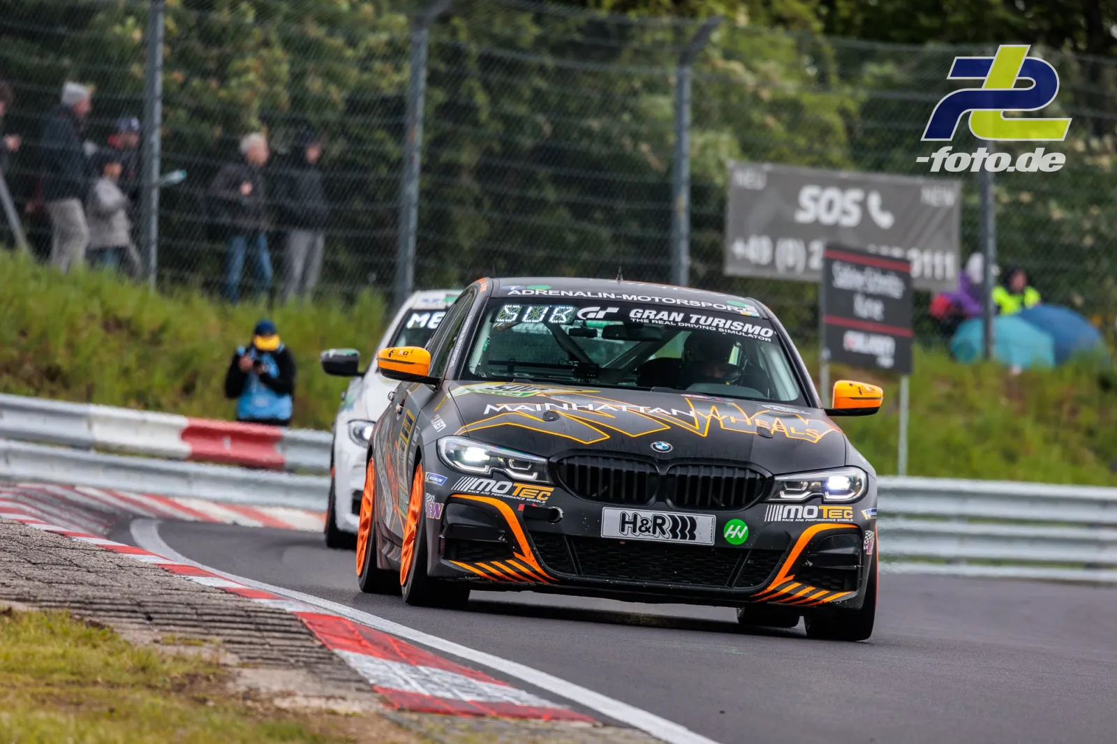 BMW Rennwagen in schwarz-oranger Lackierung auf der Nordschleife des Nürburgrings während des 24-Stunden-Rennens.