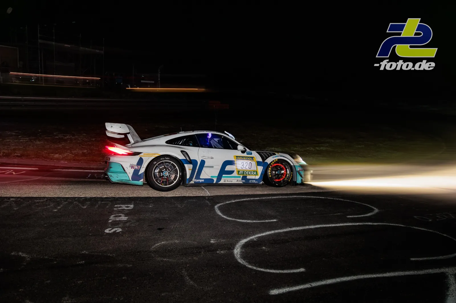 Porsche 911 GT3 R mit Startnummer 320 bei Nachtfahrt im 24h-Rennen Nürburgring, Lichtstreifen anderer Fahrzeuge im Hintergrund.