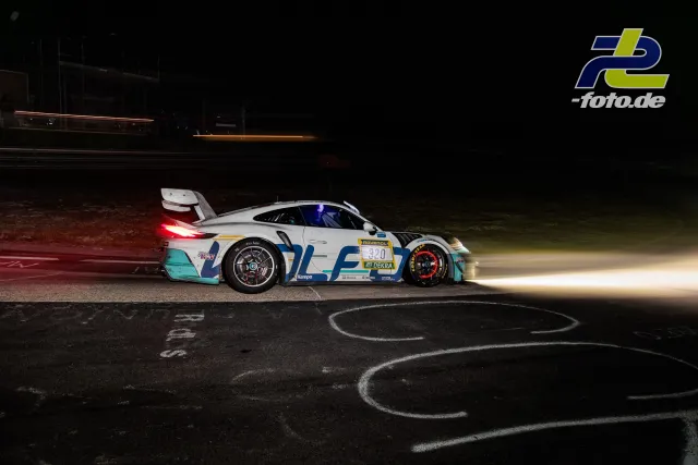 Porsche 911 GT3 R mit Startnummer 320 bei Nachtfahrt im 24h-Rennen Nürburgring, Lichtstreifen anderer Fahrzeuge im Hintergrund.