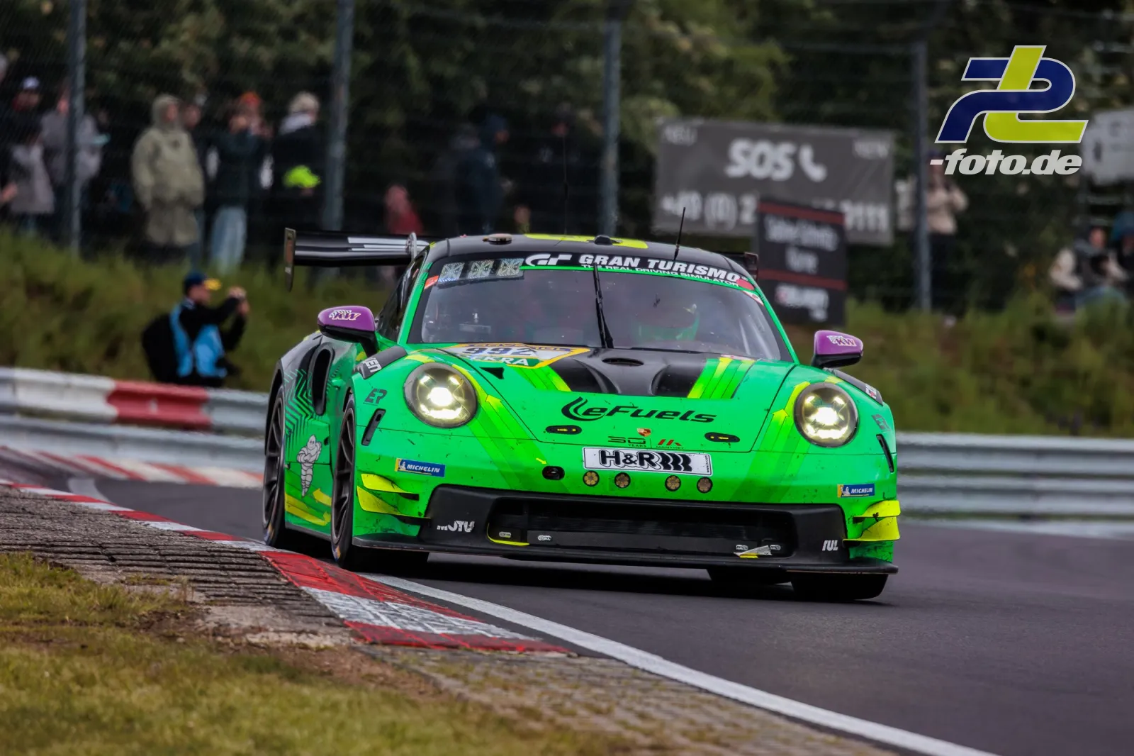 Porsche 911 GT3 R in grün-gelber eFuels-Lackierung fährt durch eine Kurve auf dem Nürburgring während des 24-Stunden-Rennens.