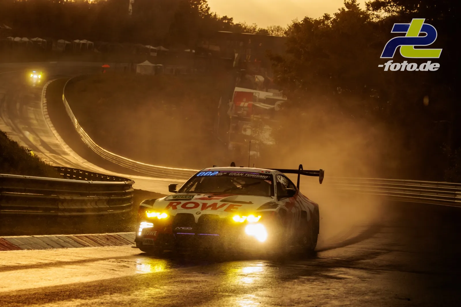 BMW M4 GT3 EVO von ROWE RACING im Gegenlicht bei Qualifying zum 24h-Rennen Nürburgring, Scheinwerfer eingeschaltet auf nasser Strecke.