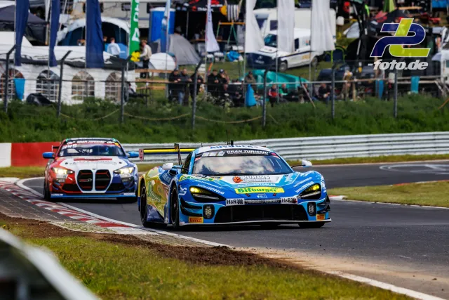 Zwei GT-Rennwagen im Zweikampf auf dem Nürburgring, vorne ein McLaren in Blau/Gelb, dahinter ein BMW M4 GT3 in Rot/Weiß/Blau.