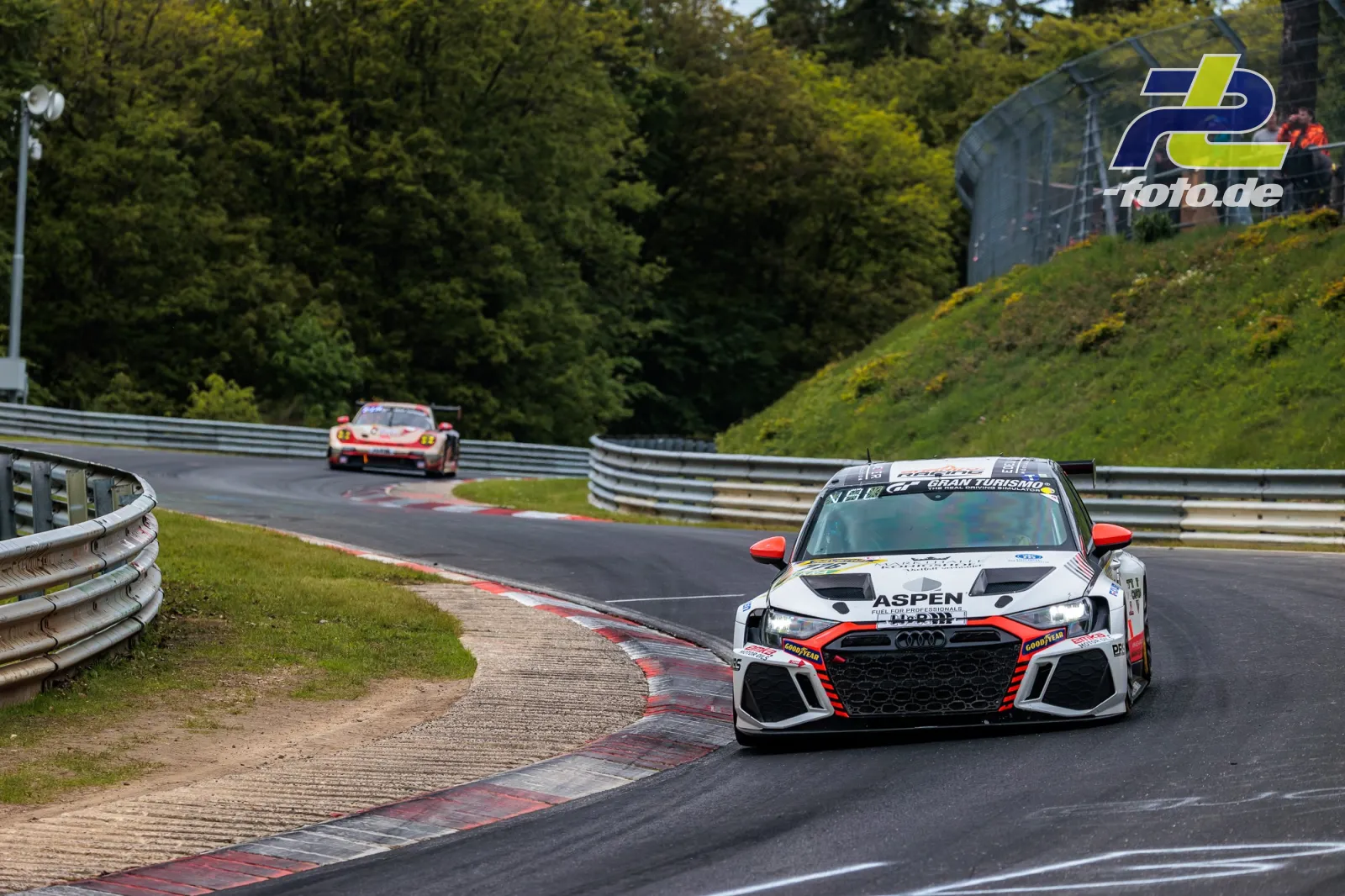 Audi auf der Nordschleife vor Porsche, Zuschauer hinter Fangzaun, typische Nürburgring-Kurvenkombination