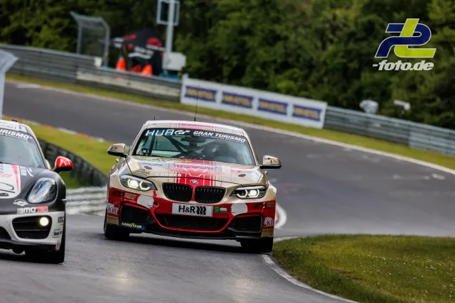 BMW M240i in rot-weißer Kariert-Lackierung während des Qualifyings auf dem Nürburgring, gefolgt von einem weißen Porsche.