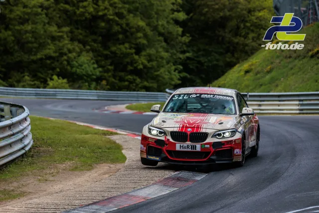 BMW im 24h-Rennen auf der Nordschleife beim Anbremsen einer Kurve mit Randsteinen und Leitplanken.