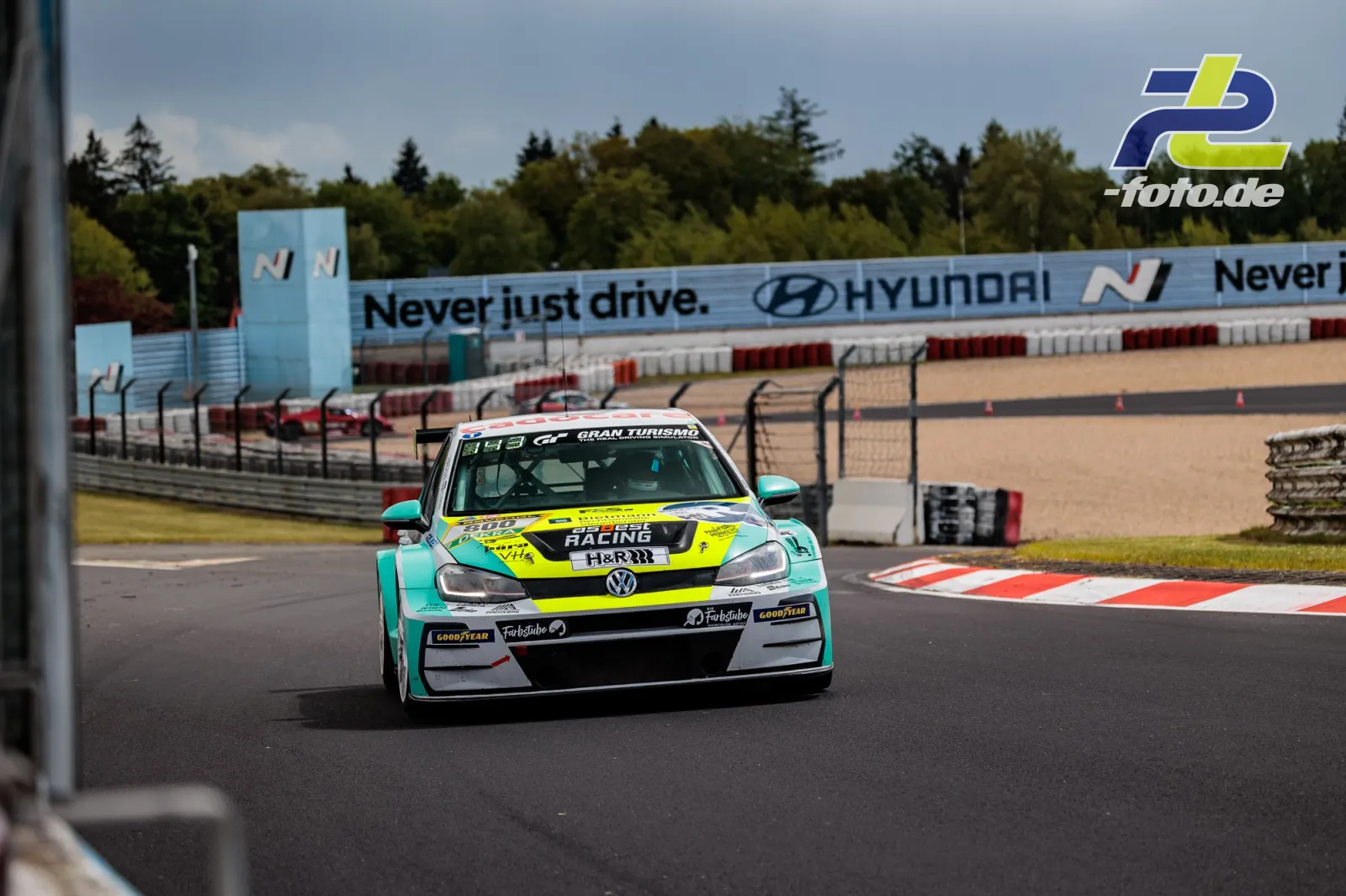 VW TCR-Rennwagen in türkis-gelber Lackierung fährt über einen Randstein auf dem Nürburgring während des Qualifyings.