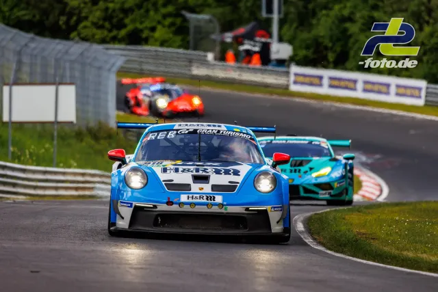 Porsche 911 GT3 R in blau-weißer H&R-Lackierung führt auf der Nordschleife vor einem türkisfarbenen Lamborghini und weiteren Fahrzeugen.