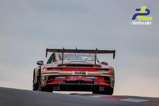 Porsche 911 GT3 R in goldbrauner und roter Lackierung von hinten über eine Kuppe am Nürburgring während des 24h-Rennens.