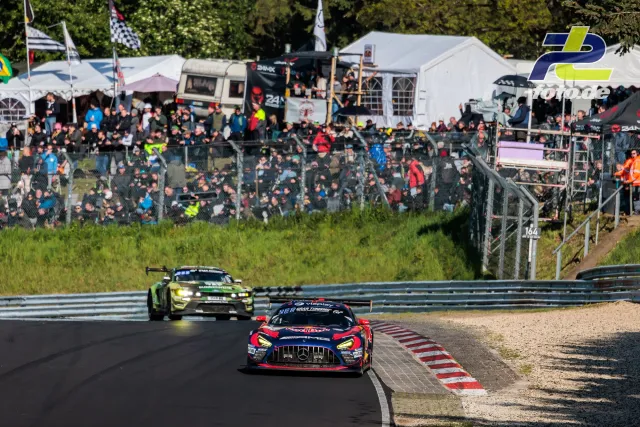 Zwei Rennwagen passieren eine Kurve vor vollen Zuschauerrängen beim 24h-Rennen Nürburgring, Streckenrandmarkierung im Vordergrund.