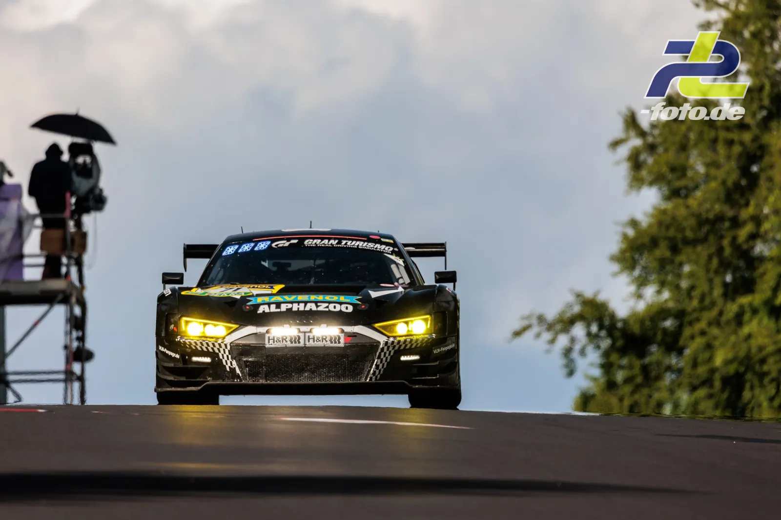 Audi R8 LMS GT3 evo II bei grauem Himmel auf der Kuppe der Nordschleife während des 24h-Rennens am Nürburgring, Streckenposten mit Schirm im Hintergrund.