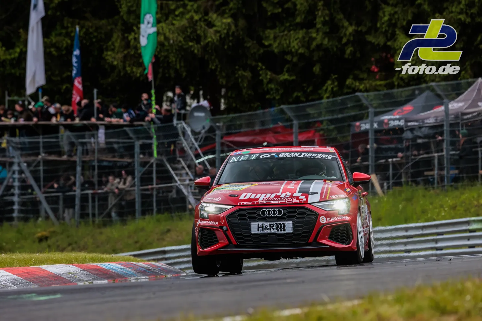 Roter Audi von Dörr Motorsport in Kurve auf Nürburgring-Nordschleife, Tribüne und Zuschauer im Hintergrund.