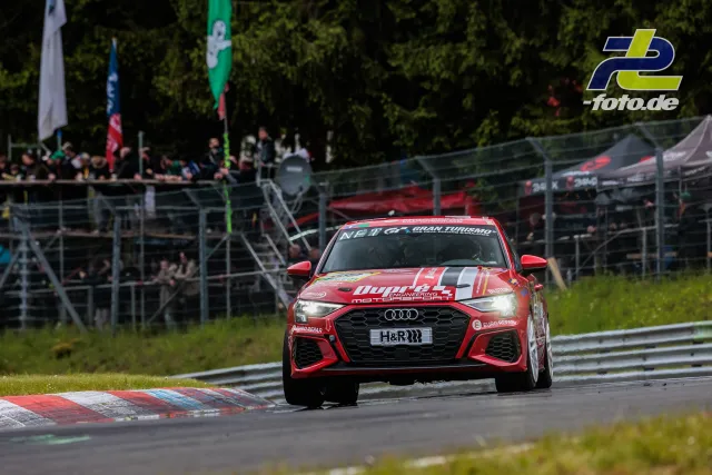 Roter Audi von Dörr Motorsport in Kurve auf Nürburgring-Nordschleife, Tribüne und Zuschauer im Hintergrund.