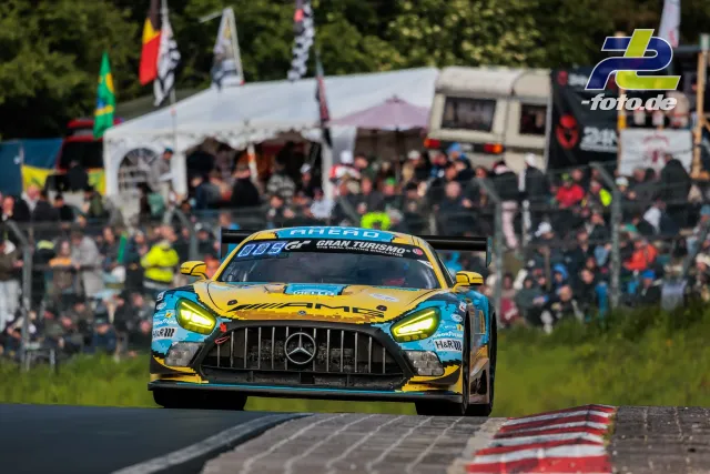 Mercedes-AMG GT3 in gelb-türkiser Lackierung vor großer Zuschauermenge am Nürburgring während des 24h-Rennens.
