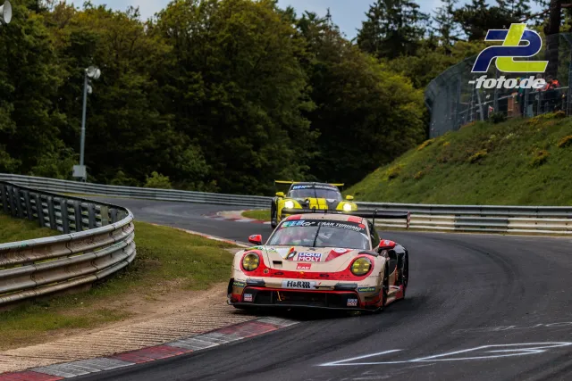 Porsche 911 GT3 R in rot-weißer Lackierung gefolgt von gelbem Rennwagen auf der Nordschleife des Nürburgring während des 24h-Rennens.