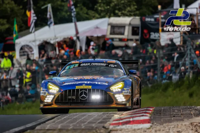 Mercedes-AMG GT3 in blau-oranger RAVENOL-Lackierung fährt über Randstein, im Hintergrund Zuschauer und Zelte am Nürburgring.