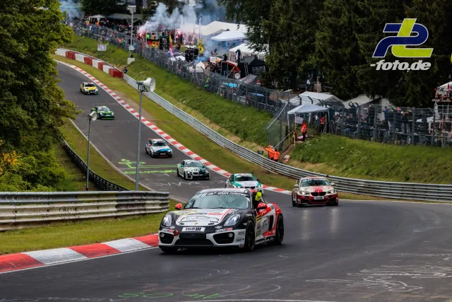 Rennfeld während 24h Nürburgring: Porsche Cayman führt Gruppe auf Nordschleife, Zuschauer mit Rauchfackeln im Hintergrund