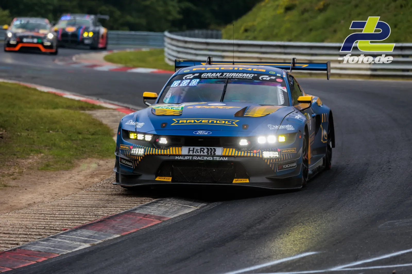 Ford Mustang GT3 EVO des HRT Ford Racing Teams in Kurve auf dem Nürburgring beim 24h-Rennen, blau-gelbe Ravenol-Lackierung.