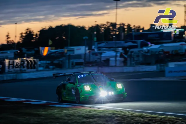 Grüner Porsche 911 GT3 R mit Startnummer 992 in der Abenddämmerung bei eingeschalteten Scheinwerfern auf dem Nürburgring.