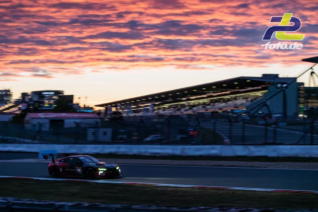 BMW M4 GT3 #77 bei Sonnenuntergang vor der Haupttribüne am Nürburgring während des 24h-Rennens