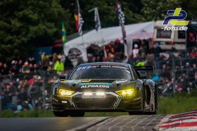 Audi R8 LMS GT3 mit gelben Scheinwerfern vor Zuschauerrängen während des 24h-Rennens am Nürburgring.