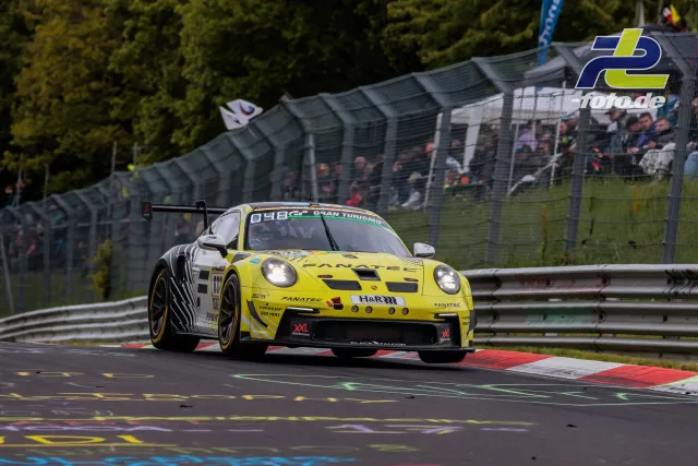 Gelber Porsche GT3 mit Startnummer 632 auf der Nordschleife während des 24h-Rennens, Zuschauertribüne im Hintergrund.