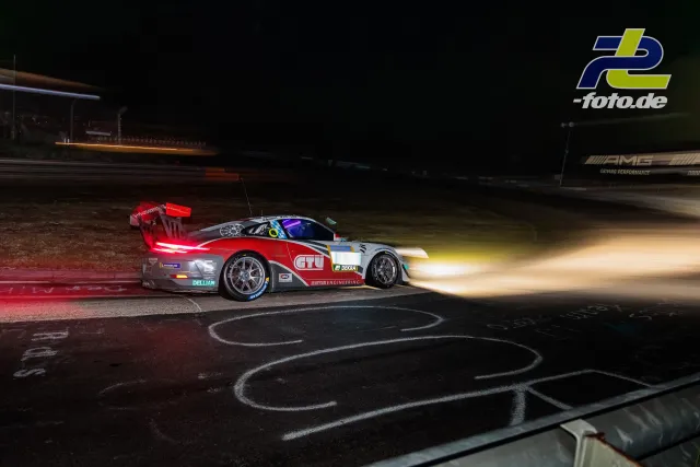 Porsche 911 GT3 Cup bei Nacht auf dem Nürburgring, rot-weiße Lackierung, beleuchtete Scheinwerfer, Kurvenausgang mit Randstein.