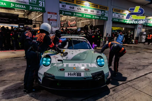 Porsche 911 GT3 R im Boxenstopp mit Mechanikern beim Reifenwechsel während des 24h-Rennens Nürburgring bei Nacht.