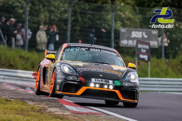 Porsche 718 Cayman GT4 in schwarz-orange auf der Nordschleife während des 24h-Rennens.