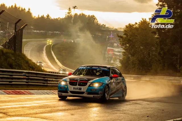 BMW 3er mit Startnummer 112 auf der Nordschleife bei Gegenlicht und aufgewirbeltem Staub, weitere Fahrzeuge im Hintergrund.