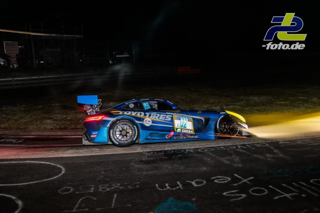 GT3-Rennwagen mit blauen Toyo-Tires-Design bei Nachtfahrt auf der Nürburgring-Nordschleife, gelbe Flammen aus dem Auspuff.