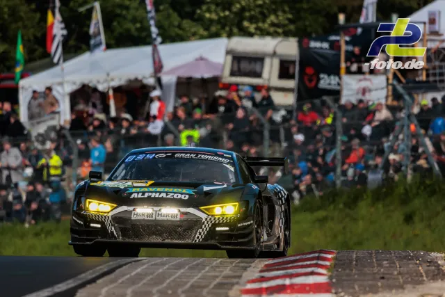 Schwarzer Audi R8 LMS GT3 mit gelben Scheinwerfern fährt vor großer Zuschauermenge am Nürburgring während des 24h-Rennens.