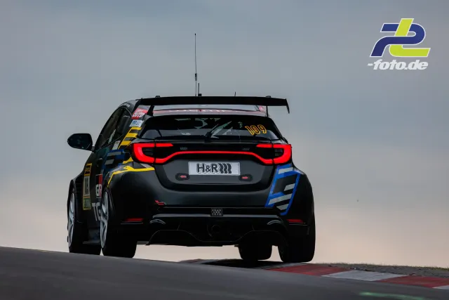 Rennwagen Nummer 109 in Heckansicht auf einer Kuppe beim 24h-Rennen am Nürburgring, schwarze Lackierung mit gelben und blauen Akzenten.