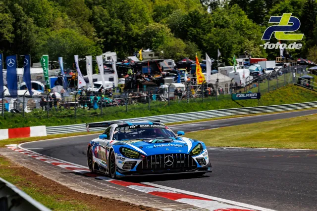 Mercedes-AMG GT3 in blau-weißer Lackierung während der Qualifikation auf der Nürburgring-Nordschleife, im Hintergrund Fahrerlager mit Zuschauern.