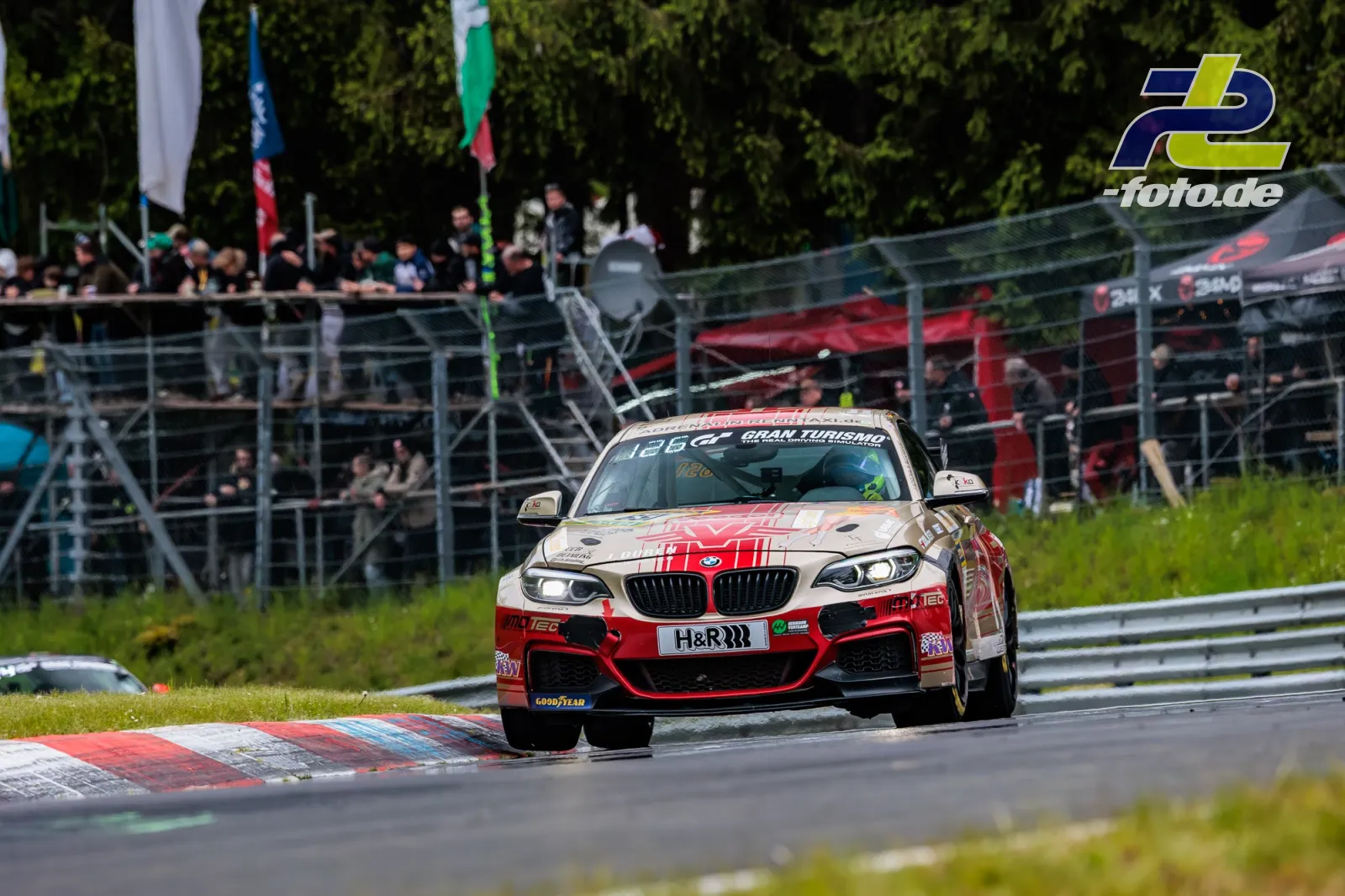 BMW M240i in rot-weißer Lackierung auf der Nordschleife des Nürburgrings, Tribüne im Hintergrund.