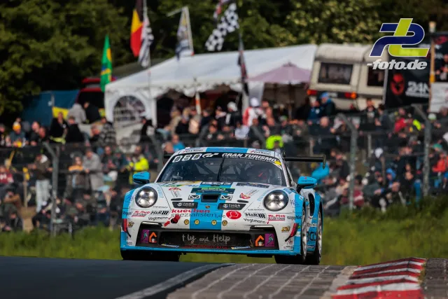 Porsche 911 GT3 R in weiß-blauer Lackierung auf der Kuppe beim 24h Rennen Nürburgring, Zuschauer im Hintergrund.