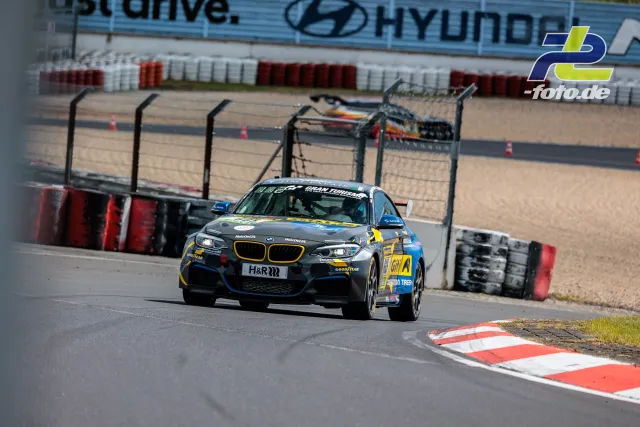 BMW M240i Racing in grau-gelber Lackierung in Kurve auf dem Nürburgring beim Qualifying zum 24h-Rennen.