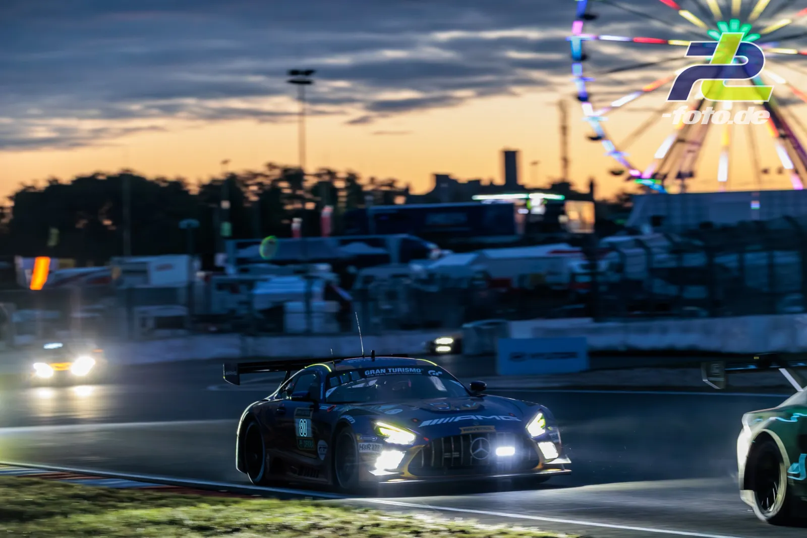 Mercedes-AMG GT3 mit Startnummer 80 im Abendlicht auf dem Nürburgring beim 24-Stunden-Rennen, beleuchtetes Riesenrad im Hintergrund.