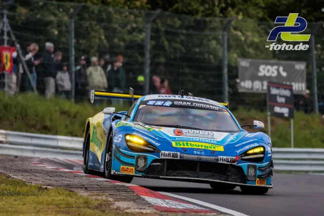 Blau-gelber McLaren 720S GT3 mit Bitburger-Sponsoring in Kurve auf dem Nürburgring, Zuschauer im Hintergrund.