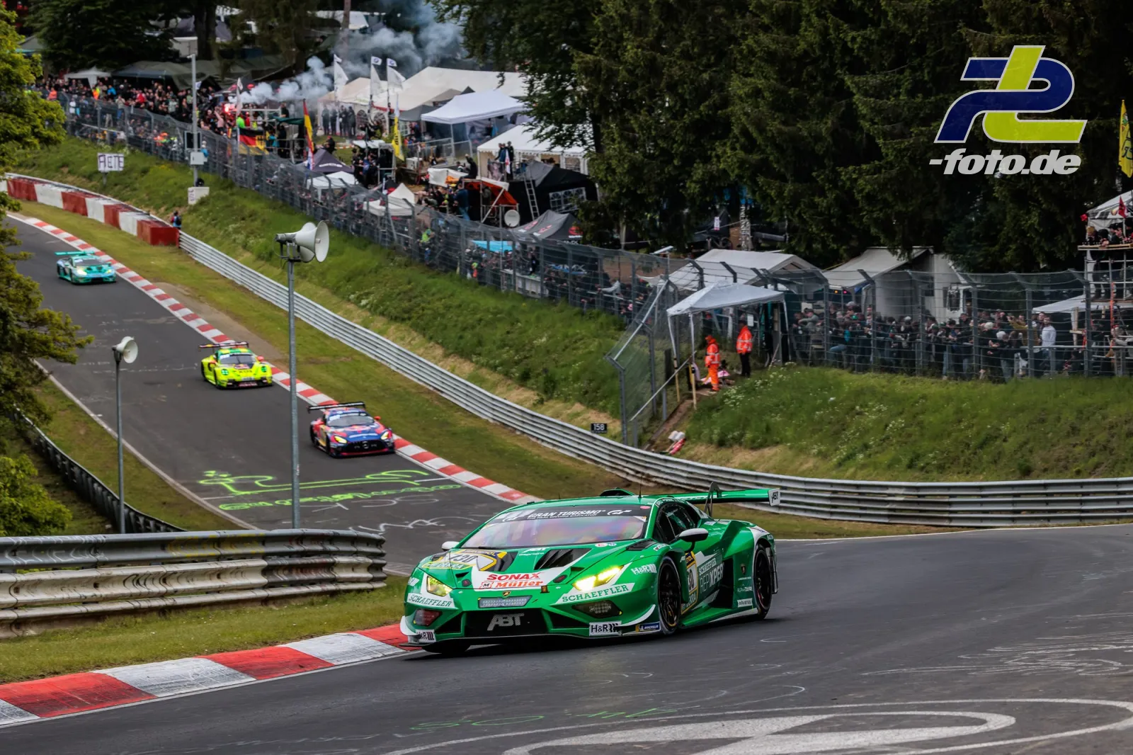 Grüner Lamborghini GT3 in der Nordschleife vor Tribünen und weiteren Fahrzeugen während des 24h-Rennens Nürburgring.