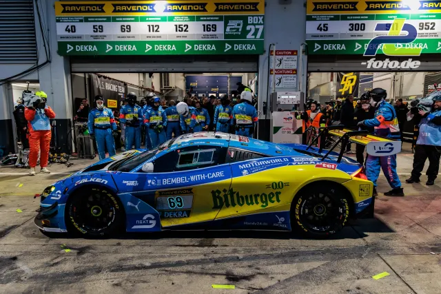 Boxenstopp bei den 24h Nürburgring: McLaren GT3 in blau-gelber Bitburger-Lackierung wird von Mechanikern umringt.